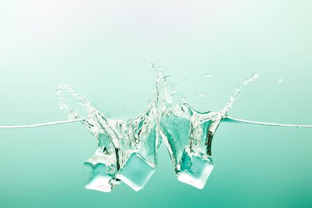 transparent pure water with splash and ice cubes on green backgroundの写真素材