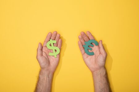 cropped view of man holding dollar and euro currency signs on yellow