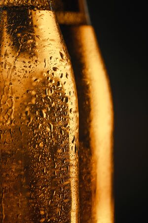 close up view of wet glass bottles of beer isolated on blackの写真素材