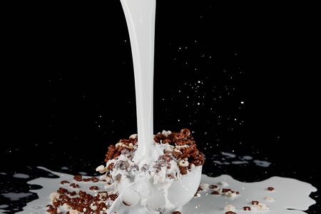 white bowl with assorted cereal with powerful milk stream isolated on blackの写真素材