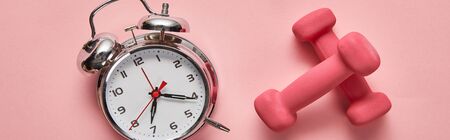 top view of silver alarm clock and pink dumbbells on pink background, panoramic shotの写真素材