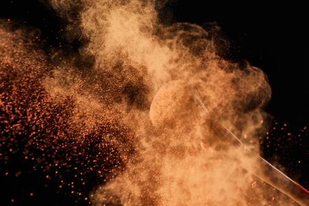 cosmetic brush with colorful orange powder explosion on black background