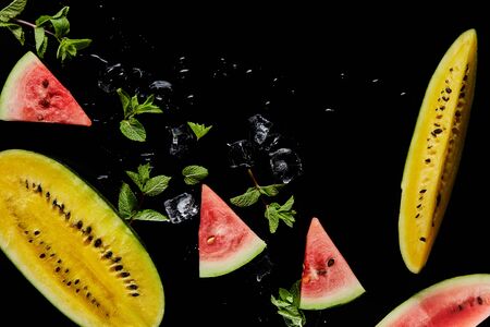 top view of red and yellow watermelon slices with mint and ice isolated on blackの写真素材