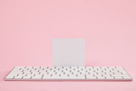 blank white card near computer keyboard on pink backgroundの写真素材