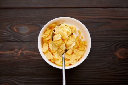top view of spoon with cornflakes above bowl on wooden surfaceの写真素材
