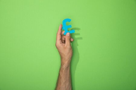 cropped view of man holding paper icon of pound currency sign on green