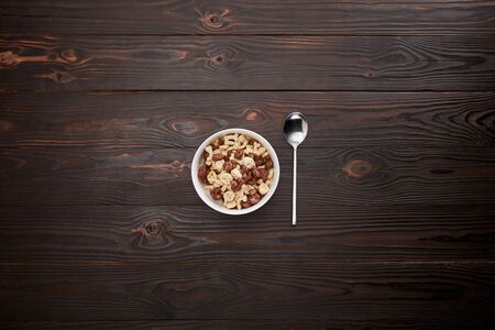 Top view of spoon near cereal in bowl on wooden surface