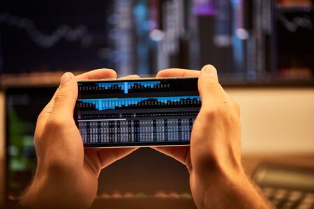 cropped view of man holding smartphone with graphs and charts