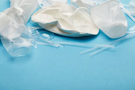 crumpled white and transparent plastic cups and plates on blue background