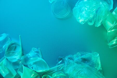 top view of crumpled plastic bags, cups, straws and forks in blue light