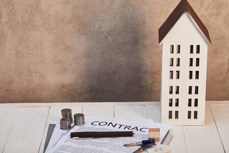 house model on white wooden table with contract, coins and keys near brown wall, real estate conceptの写真素材