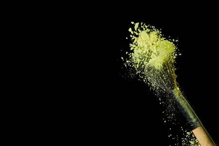 cosmetic brush with yellow powder explosion on black background