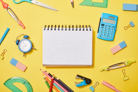 top view of blank notebook among school supplies on yellow backgroundの写真素材