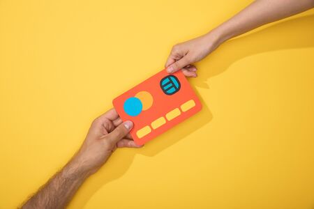 cropped view of man and woman holding paper icon of credit card on yellowの写真素材