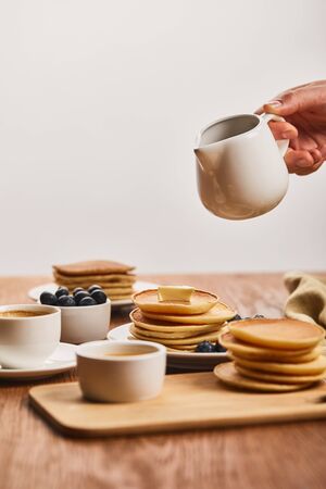 cropped view of man holding jug with syrup upon plate with pancakes and blueberries near cup of...