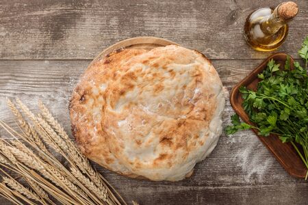 top view of lavash bread near wheat spikes, fresh parsley and olive oil on wooden table