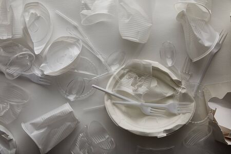 top view of crumpled disposable plates, plastic cups, forks and spoons on white background
