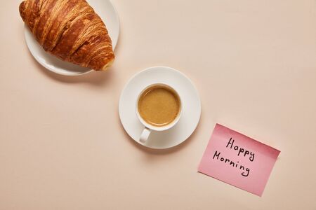 flat lay with coffee, croissant and sticky note with happy morning lettering on beige backgroundの写真素材
