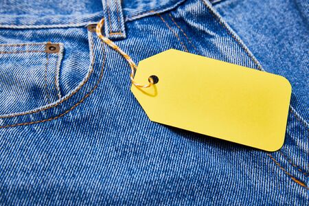 close up view of yellow paper sale tag on rope on jeans