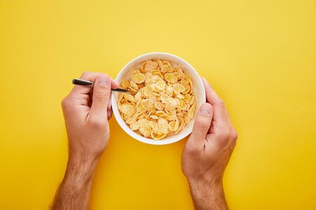 cropped view of man holding bowl with cornflakes isolated on yellowの写真素材