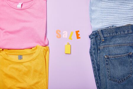 top view of sale lettering above shopping paper bag near colorful clothes on violet