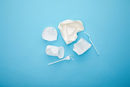 top view of pile of white disposable cups, forks and plate on blue background