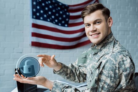happy military man gesturing in office near virtual padlock and laptopの写真素材