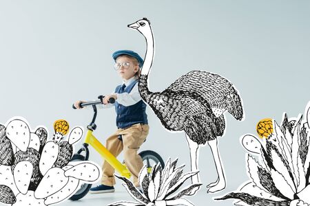 thoughtful kid in retro vest and cap riding bicycle on grey background with fairy ostrich among cacti illustrationの写真素材