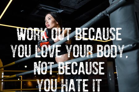 low angle view of attractive woman in boxing gloves standing in sports center with work out because you love your body, not because you hate it illustrationの写真素材