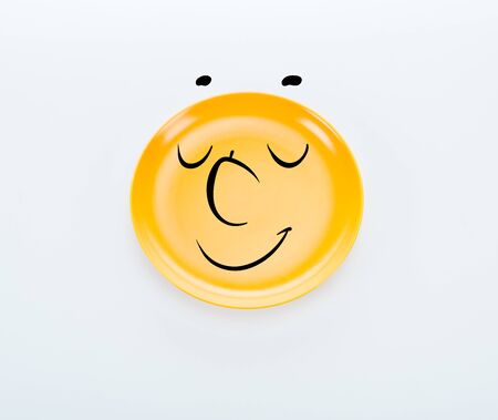 top view of shiny yellow plate with pleased smiley on white backgroundの写真素材