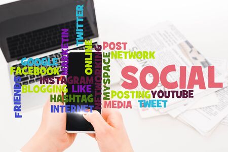 selective focus of woman holding smartphone near laptop and newspapers with social media illustrationの写真素材