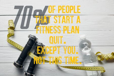 top view of bottle with water, measuring tape and dumbbells on wooden white background with 70% of people that start a fitness plan quit, except you, not this time illustrationの写真素材