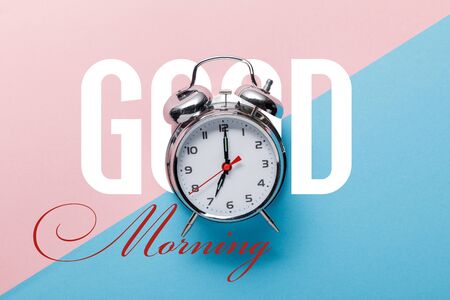 top view of classic silver alarm clock on pink and blue background with good morning letteringの写真素材