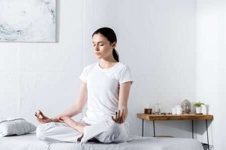 young woman sitting in lotus pose with closed eyes on massage tableの写真素材
