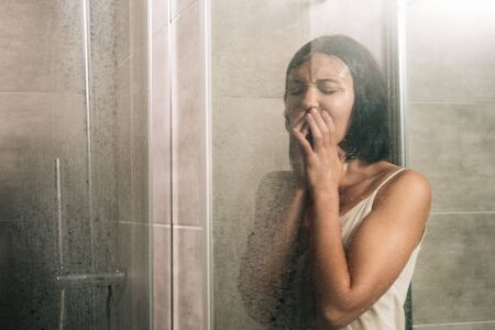 lonely depressed woman covering mouth and crying in shower at homeの写真素材