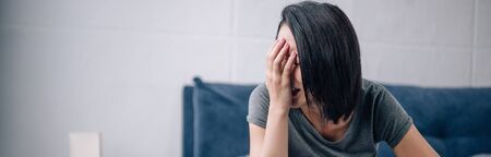 panoramic shot of upset lonely brunette woman covering face at home
