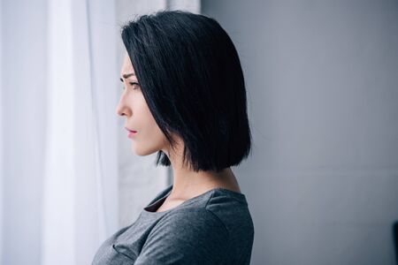 beautiful depressed woman looking at window at home with copy space