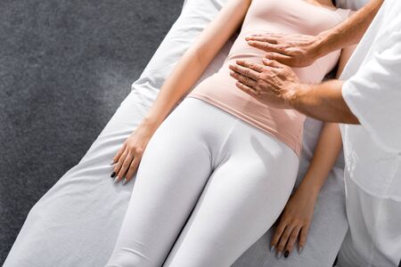 cropped view of healer standing near woman and holding hands above her stomach