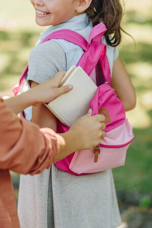 partial view of schoolboy packing book in backpack of smiling schoolgirlの写真素材