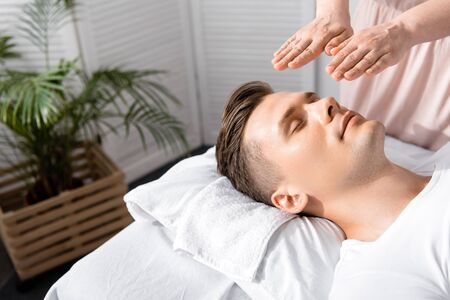 cropped view of healer standing near man with closed eyes and holding hands above his headの写真素材