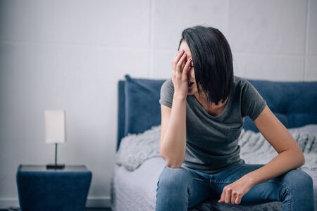 depressed woman sitting on bed at home and crying