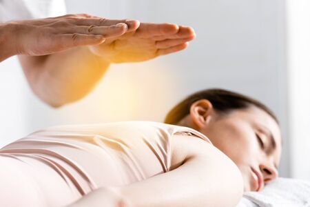 cropped view of healer standing near woman lying with closed eyes and holding hands above her bodyの写真素材