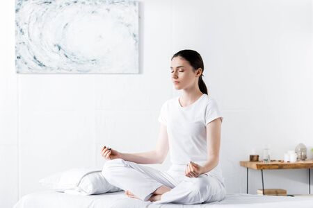woman sitting on massage table in lotus pose with closed eyesの写真素材