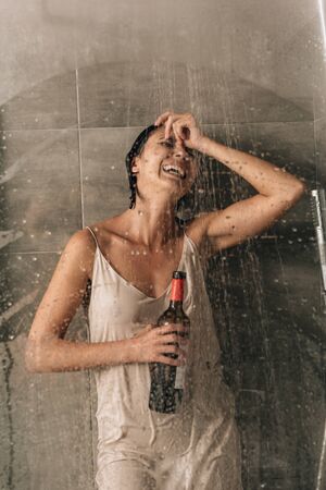 lonely depressed woman in shower holding wine bottle and crying at homeの写真素材