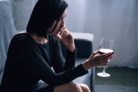 depressed woman sitting on sofa with wine glass at homeの写真素材