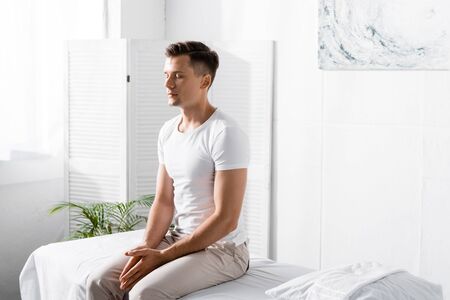 man in white t-shirt sitting on massage table with closed eyes in clinic