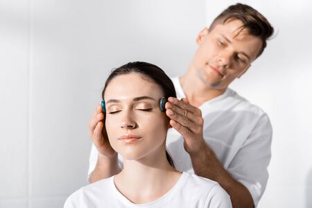 healer standing near woman with closed eyes and using stones