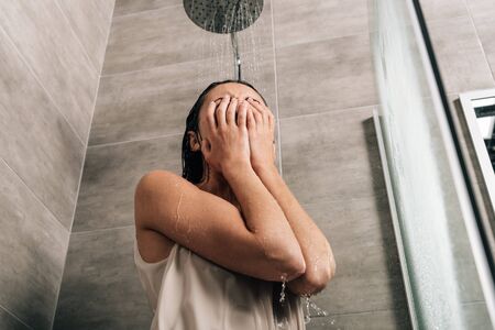 depressed woman covering face with hands while crying in shower at homeの写真素材