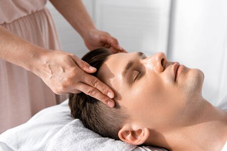 cropped view of masseur standing near man with closed eyes and touching his headの写真素材