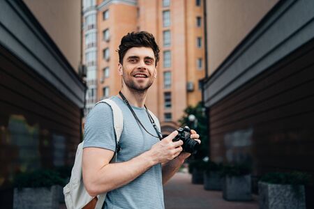 handsome man in t-shirt holding digital camera and looking awayの写真素材